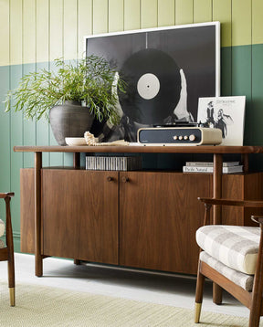 Lifestyle of the Walnut Grove Credenza against a dark green and light green wall, with a plant and record player above it and large picture of hands holding a record leaning against the credenza and wall.
