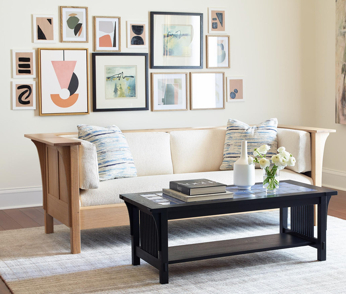A white fabric Settle sofa and black coffee table sit in front of a wall covered with picture frames of varying sizes with abstract art
