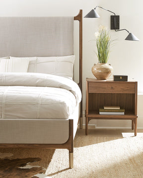 Walnut Grove nightstand and light gray upholstered bed that is cropped to only show half of the bed on top of a tan rug