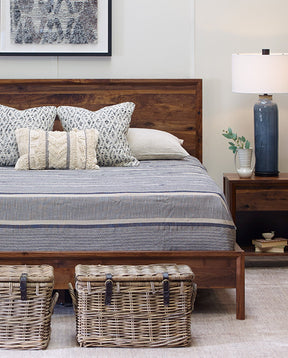 Lifestyle of a Fulton Lane Beckett Bed with a blue striped quilt on top of the bed and two woven wicker baskets in front of the bed