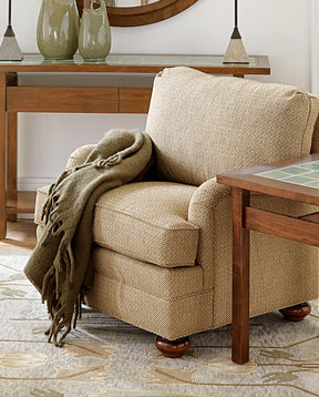 Lifestyle of a light brown fabric 7000 Series arm chair with a dark green throw blanket draped over an arm. There is a Mission Tile-Top End Table next to the chair