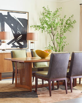 A Park Slope dining table surrounded by green upholstered Park Slope chairs, with a matching sideboard in the background that has an abstract black and white painting above it