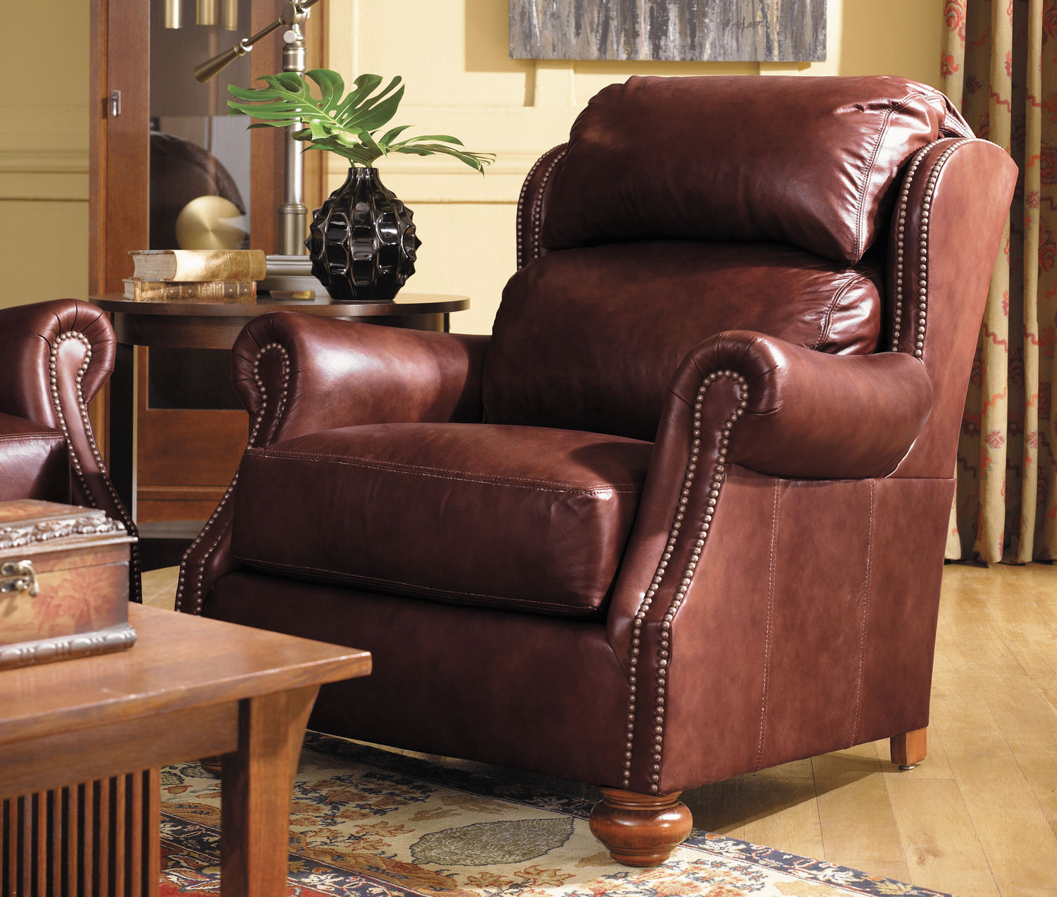 Lifestyle of a brown leather Durango Recliner that has a wooden end table next to it with a small black vase on top, and the corner of a Park Slope coffee table is shown in the bottom left corner