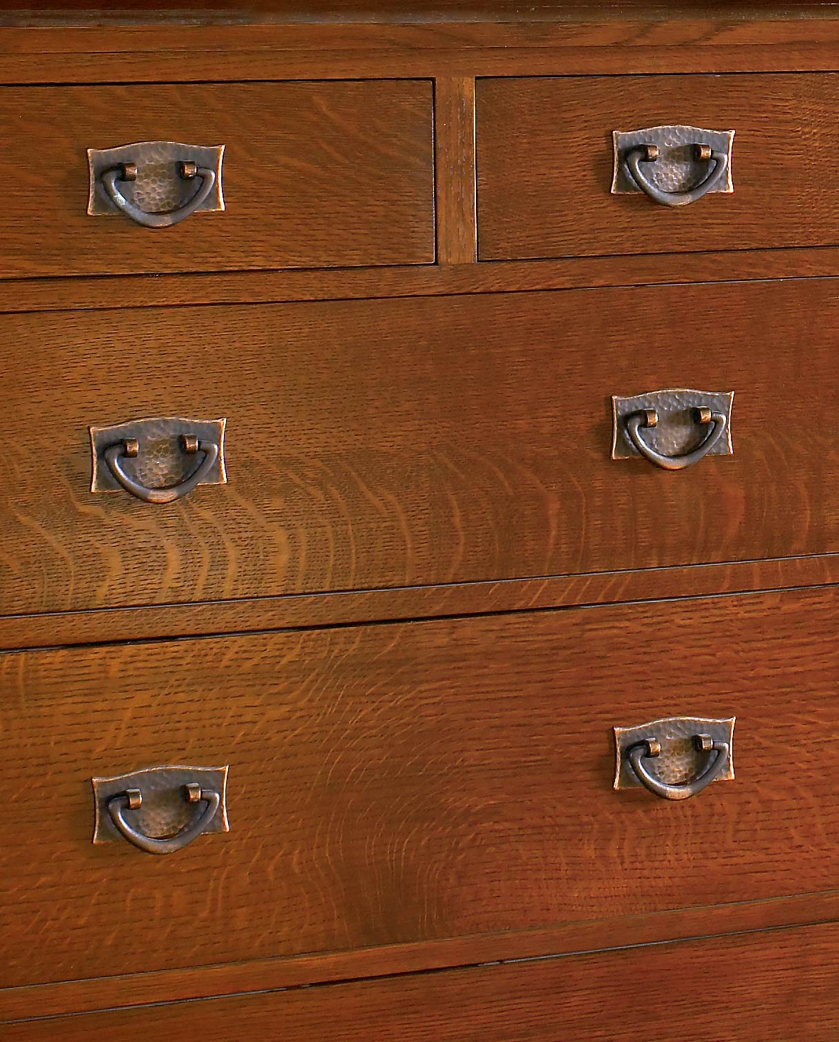 A closeup of an oak drawer front with dark copper bail pulls