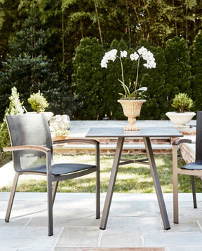 An outdoor patio set up showing a stone top table and two chairs, the chair on the right is cut off