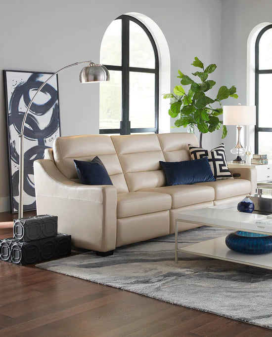 American Leather living room set up, showcasing a tan colored leather couch with dark blue accent pillows, a lamp beside the couch, and a coffee table in front