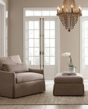 Stickley Accent Chair and Ottoman in light brown fabric in a cream colored room with a dark gold chandelier above it