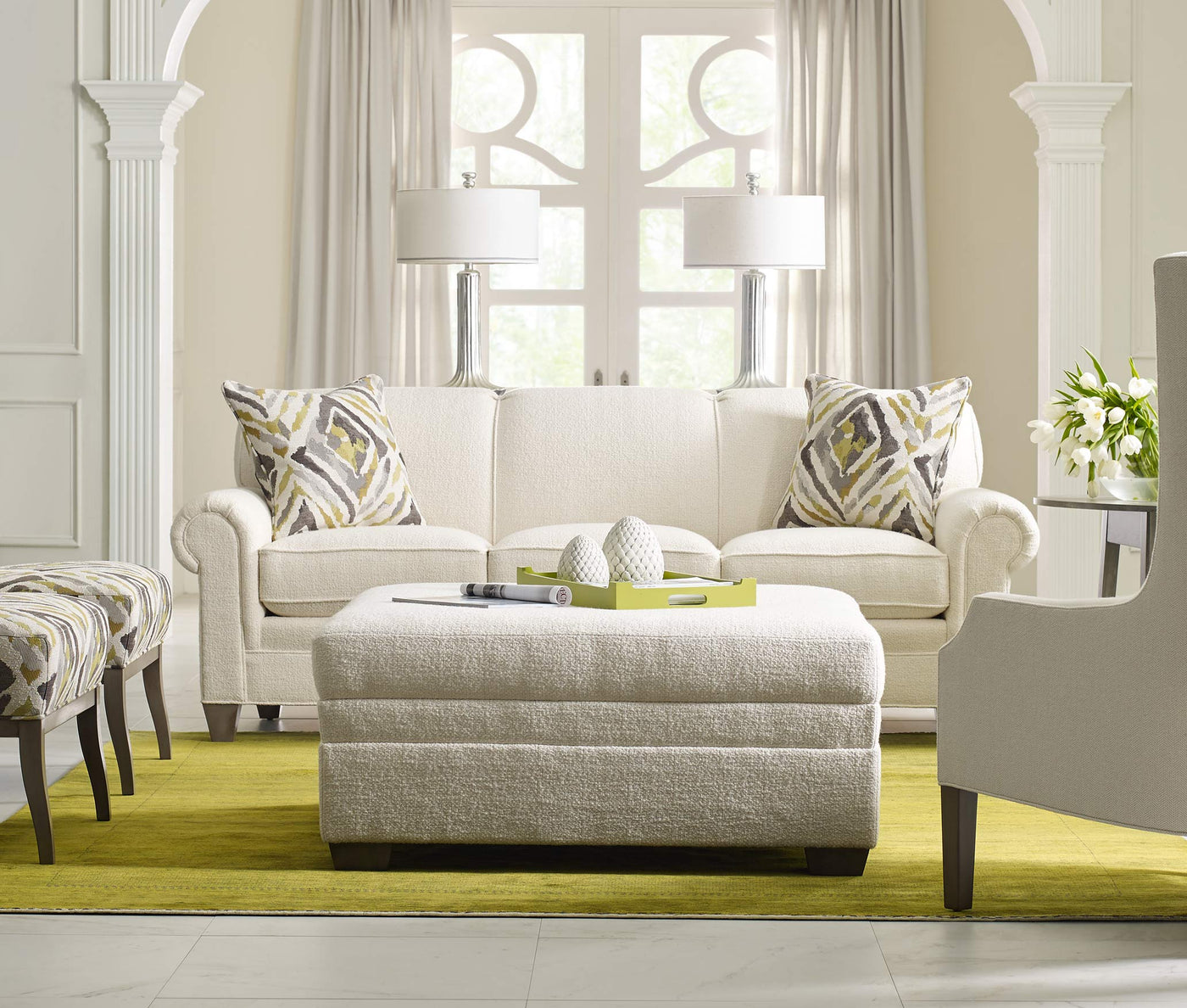 Cream colored Stickley 7000 Series sofa with white, gray, and green decorative pillows and ottoman with a light green rug underneath