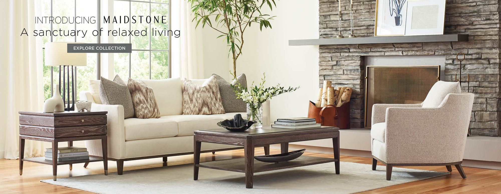 Lifestyle of the Maidstone Sofa, accent chair, side table, and cocktail table. They are sitting in front of a stone fireplace with a large window behind the sofa letting in natural light. The image has text on it reading "Introducing Maidstone. A sanctuary of relaxed living. Explore collection."