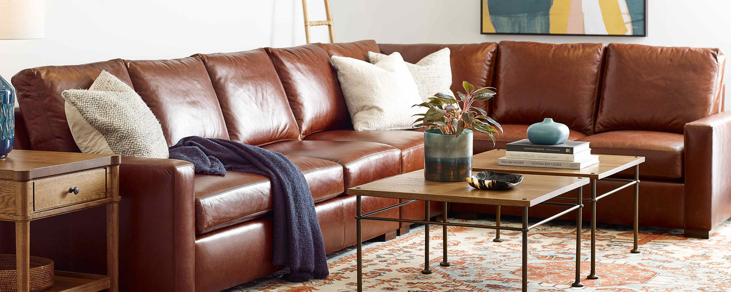 Lifestyle of a brown leather Memphis sectional, there is a dark blue throw blanket draped on a cushion and three white accent pillows