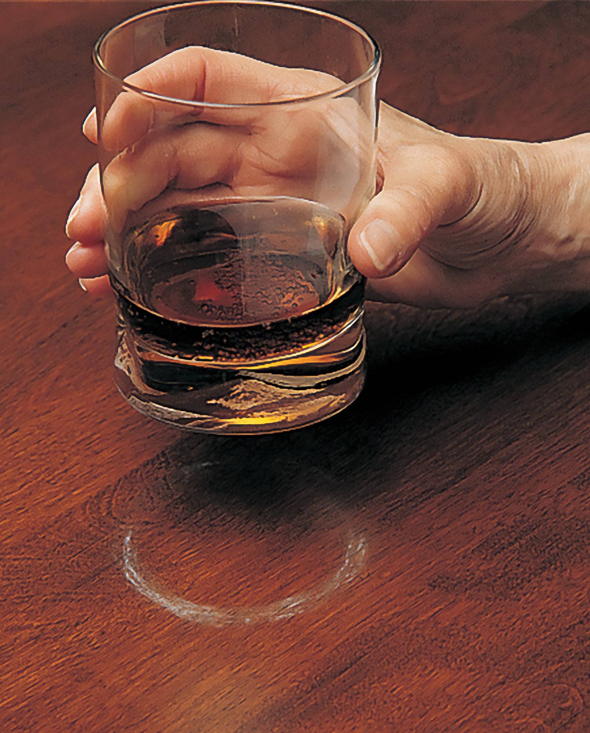A hand holding a glass of liquid showing a ring wet ring on a table