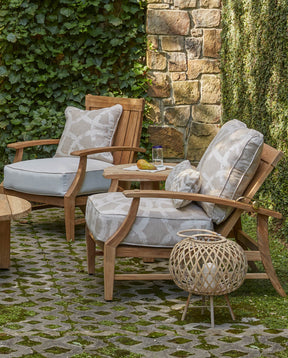 Outdoor Croquet Teak Lounge Chair in Natural Teak sit against a stone wall covered in vines
