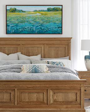 A blue and green colorful painting of a grassy pond is displayed on a white wall above a St. Lawrence bed.