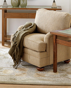 A light tan upholstered chair with a dark green throw blanket on it sits on top of an Ivory Rennie Tulip rug