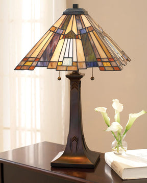 A Stained Glass lamp sits on top of a dark wood table next to a tiny vase with four small white flours in it