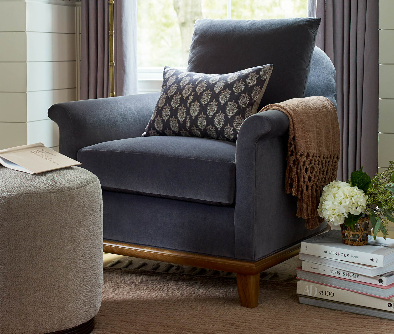Lifestyle of a navy blue fabric Martine Chair with a printed accent pillow on it and a brown throw blanket draped over one arm