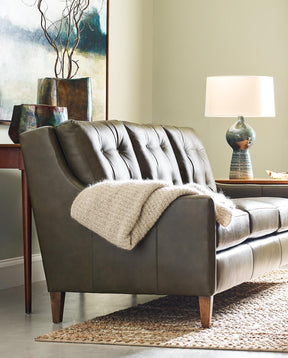 Lifestyle of a gray leather 500 Series Three Cushion Sofa with a cream throw blanket over the arm, there is a patterned fabric accent Chair next to it and a coffee table in front of both 