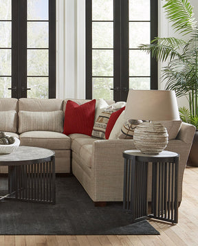 Lifestyle of a light brown fabric 7000 Series Sectional that has brown and red accent pillows. There is a Park Slope round end table next to the sectional with a found base lamp on the end table