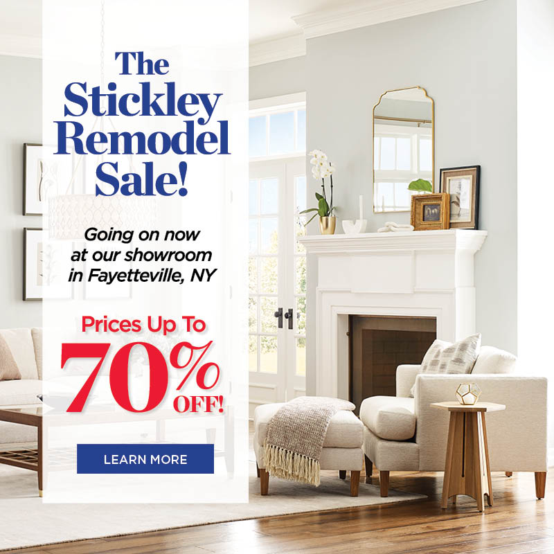 Lifestyle image of a cream colored sofa and accent chair with an ottoman in front of it. There is a Surrey Hills coffee table and side table with the furniture. A white banner with red and blue text reads: "The Stickley Remodel Sale! Going on now at our showroom in Fayetteville, NY. Prices up to 70% off. Learn more."