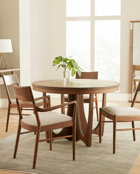 A Walnut Grove Round Dining Table is surrounded by four Walnut Grove Chairs in a cream colored room that has one floor to ceiling window