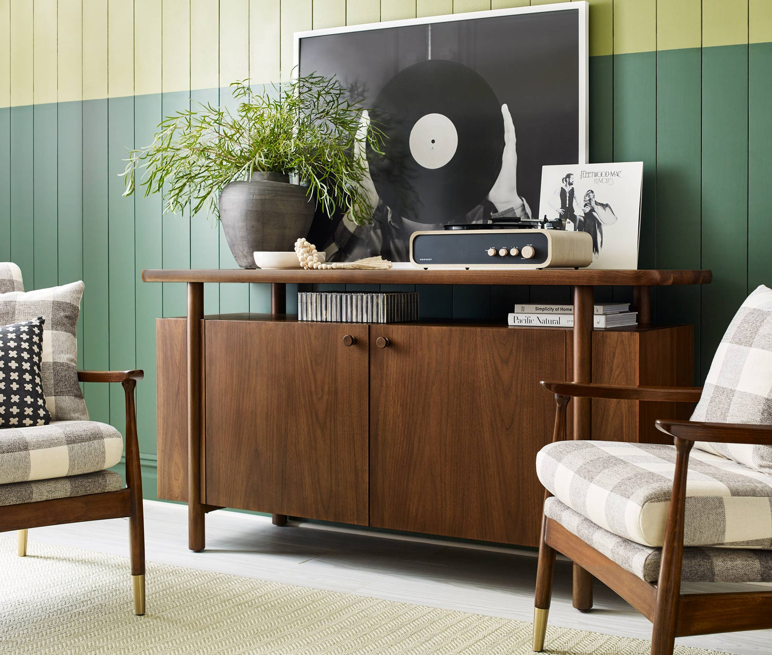 Lifestyle of a Walnut Grove Credenza that has a record player and large potted plant on top of it, it is against a dark green and light green paneled wall with two Walnut Grove chairs in front of it